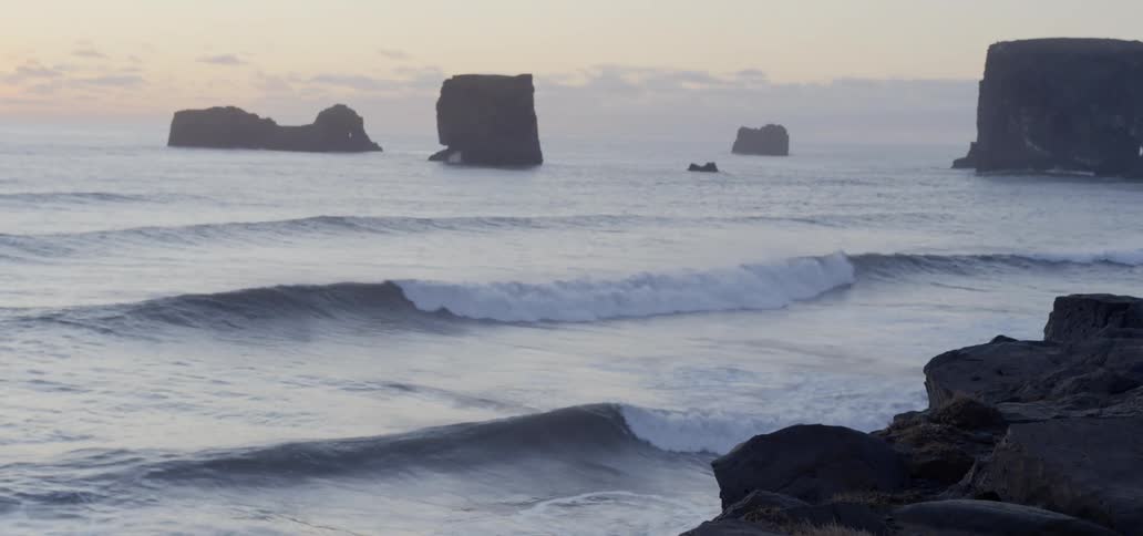 Waves rush into the shore and crash into rocks at dusk
