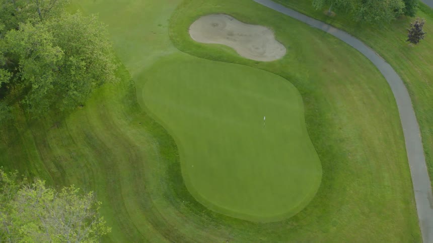 A flag on a pole marks the hold on the green near a sand trap on a golf course
