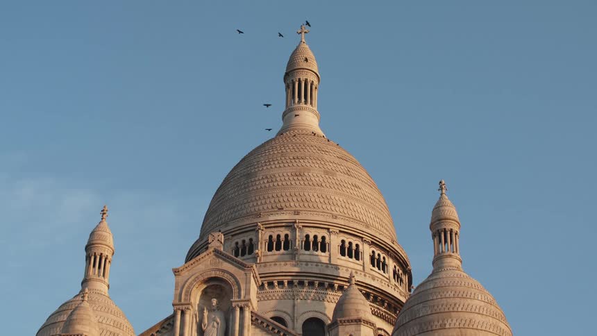 Birds flying around a cross on the top of the dome of a cathedral Montmartre Paris