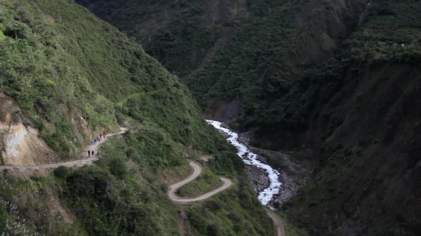 Many people walking on a winding dirt path in a mountainous area