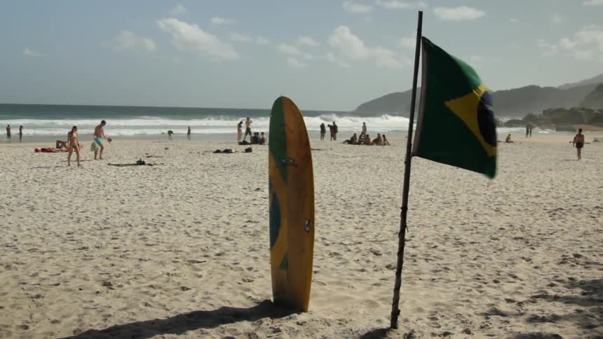 A surfboard and flag are in the sand of a beach