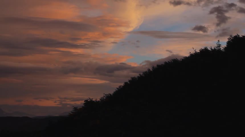 A hillside has heavy clouds and a sun setting