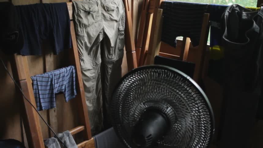A fan blowing on clothing hung on a drying rack