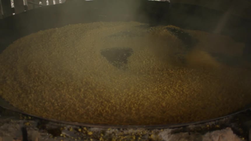 A person is mixing something in a large heated vat