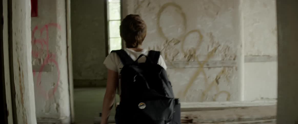 A teenager walks through an abandoned building covered with graffiti