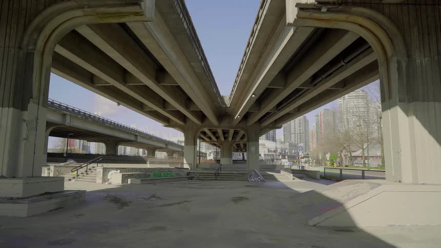 A passenger train travels beneath a concrete overpass in a city