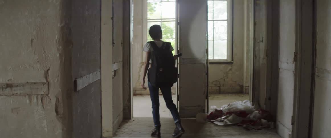 Female enters an abandoned building and looks around at the damage with a flashlight