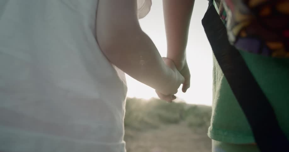 Siblings hold hands as they walk on a dirt trail on a sunny day