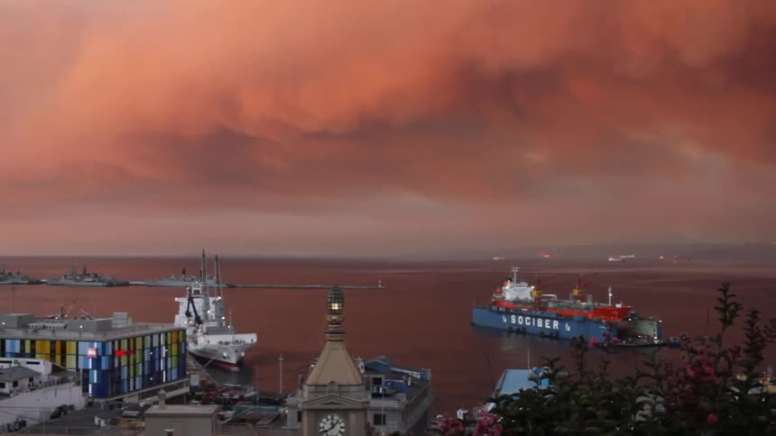 A harbor with boats and buildings under a red sky full of storm clouds