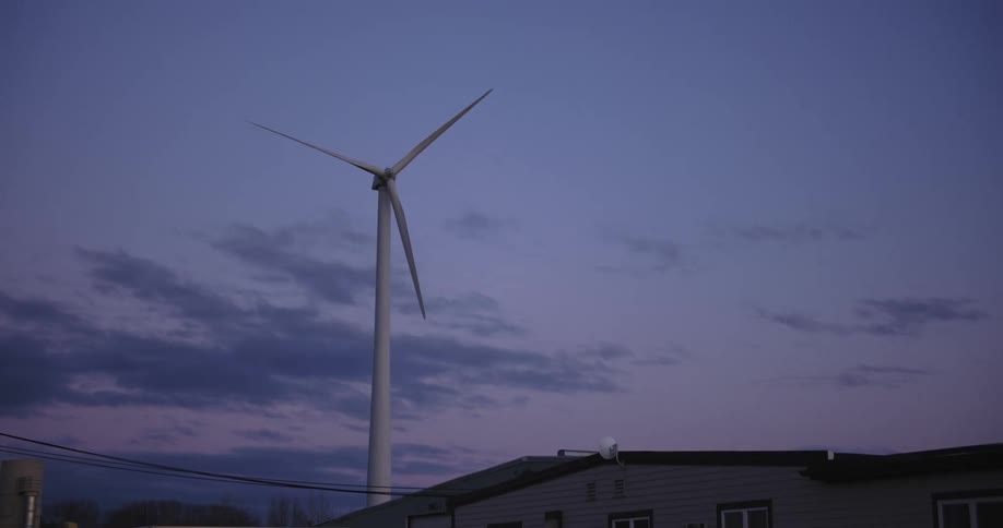 The blades of a wind turbine turn slowly at dusk