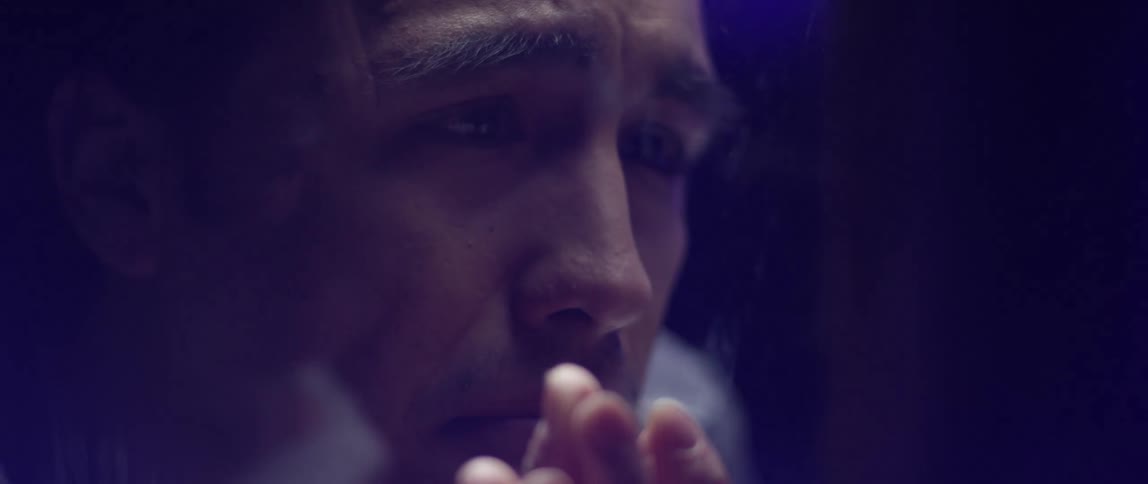 A man looks sadly at his wife while touching the glass barrier between them