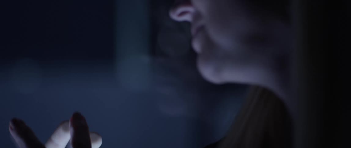 A woman reaches her hand up to a glass divider and looks at someone on the other side