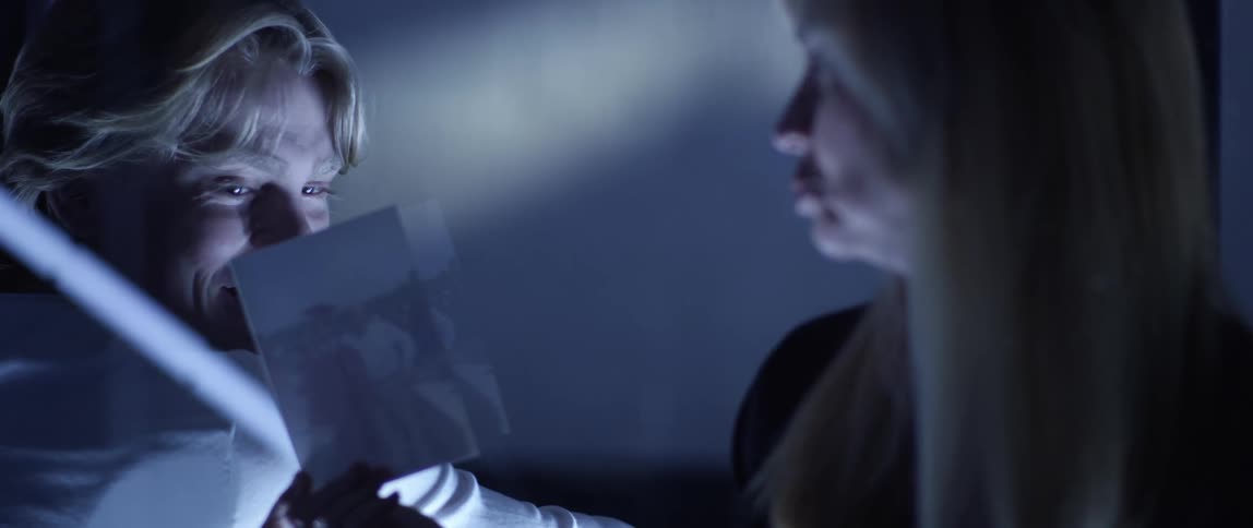 A blonde woman holds up a photograph for a man to look at