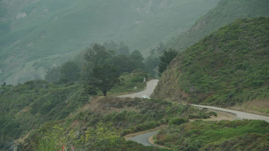 Aerial of car driving on windy road through the mountains on a cloudy day