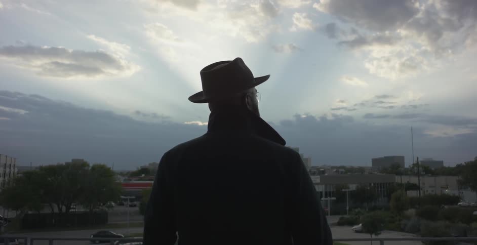 A man stands overlooking a city area with clouds overhead