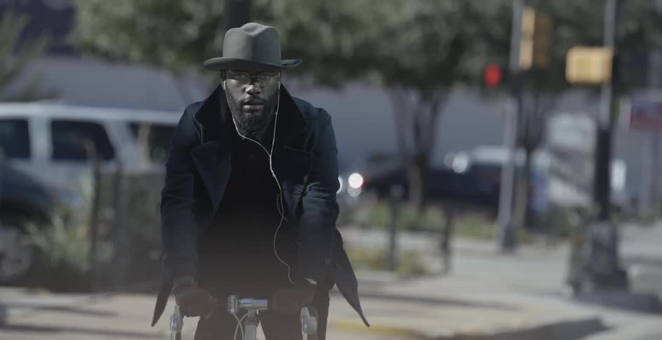 A man wearing a hat and earbuds rides a bicycle