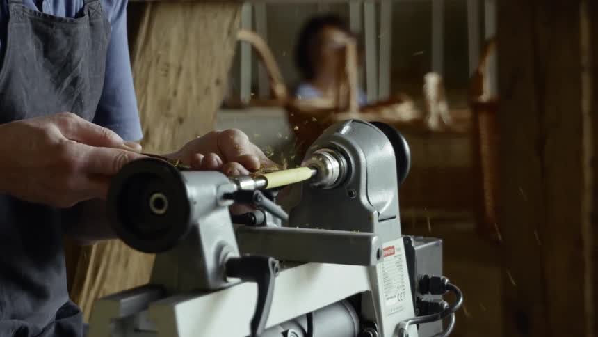 Person shapes wood spinning on machine in workshop