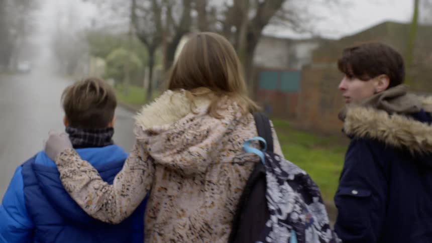Three young white people walk slowly down a rain covered street