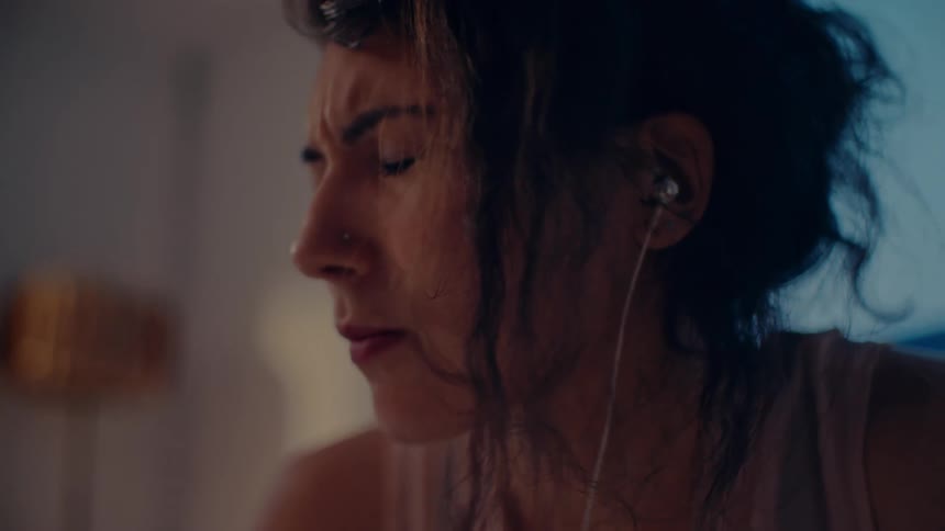 Woman intensely listens to music with earbuds in bedroom