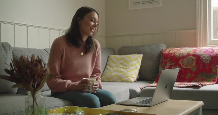 A white woman sits on a couch and talks to someone through a laptop