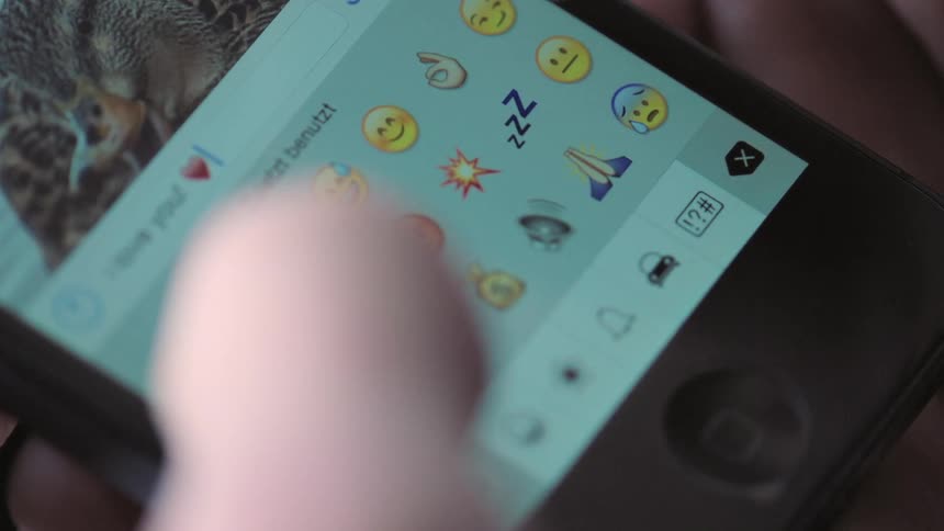 Persons fingers hover over emoji on mobile phone screen