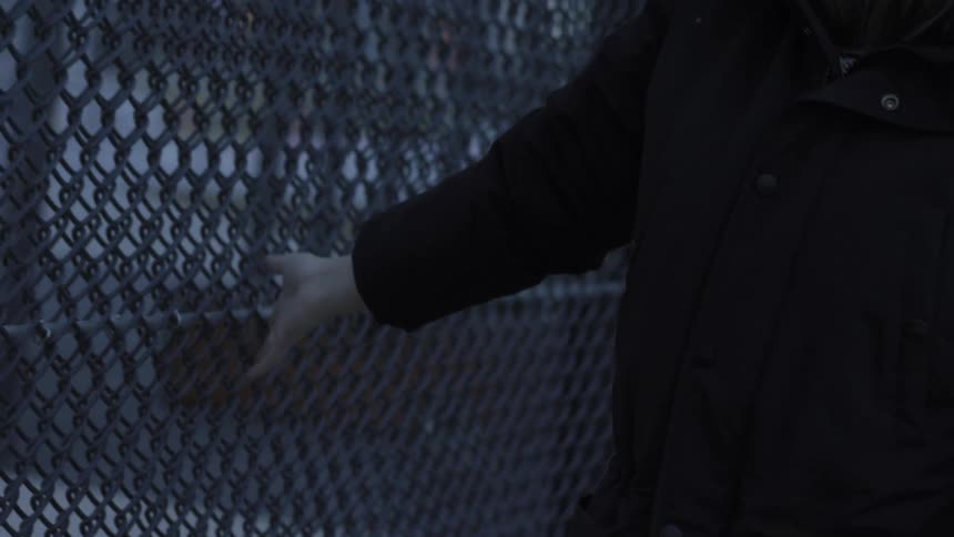 A woman walks and runs her hand along a chain link fence