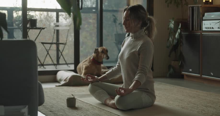 A woman meditating on a mat in the living room of a house
