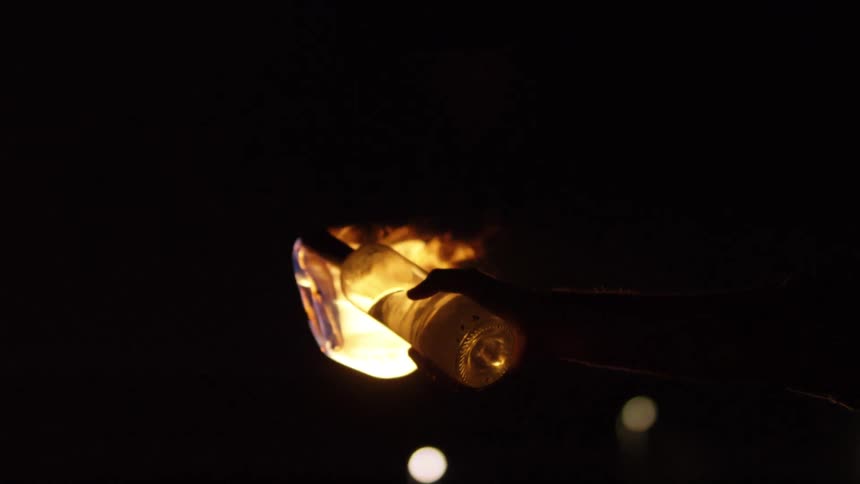 A person waves a bottle with a burning piece of cloth in it in the air
