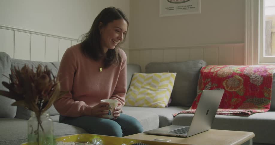 A woman is sitting on the couch talking to someone through her laptop
