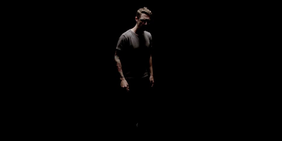 A white man stands in shadow while extending his arm forward