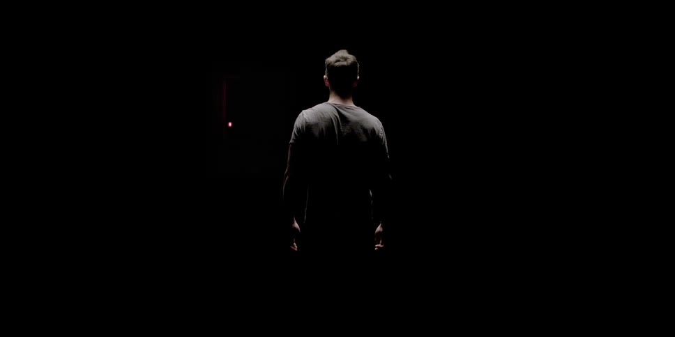 A man walks towards a red door that slowly opens in a black room