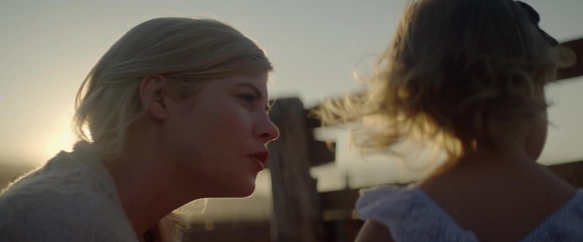 Mother talks to daughter near wooden fence as sun hovers on the horizon