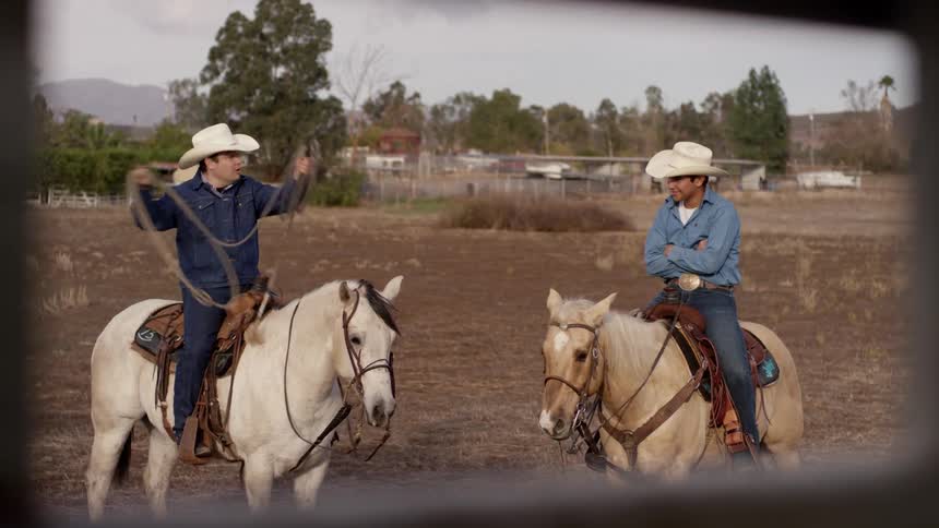 A cowboy shows his lasso to another cowboy