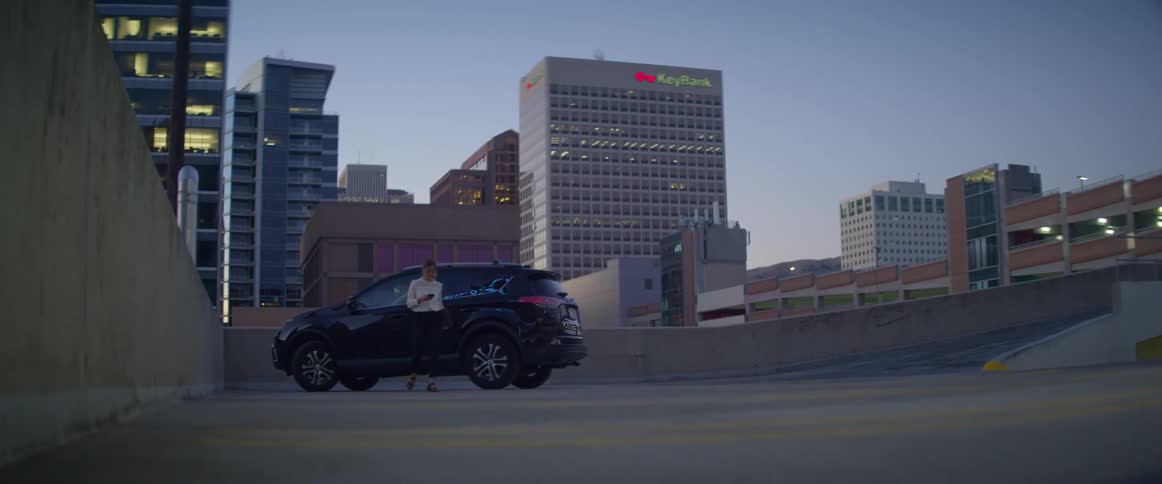 A woman parked on the rooftop of a large building gets out of her vehicle