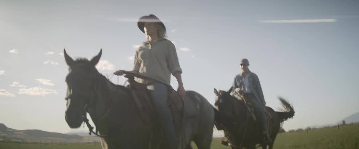 Woman and man ride horses through open fields