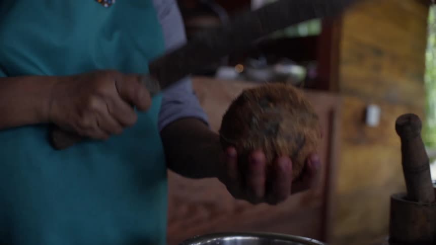 A man uses a large knife to cut open a coconut