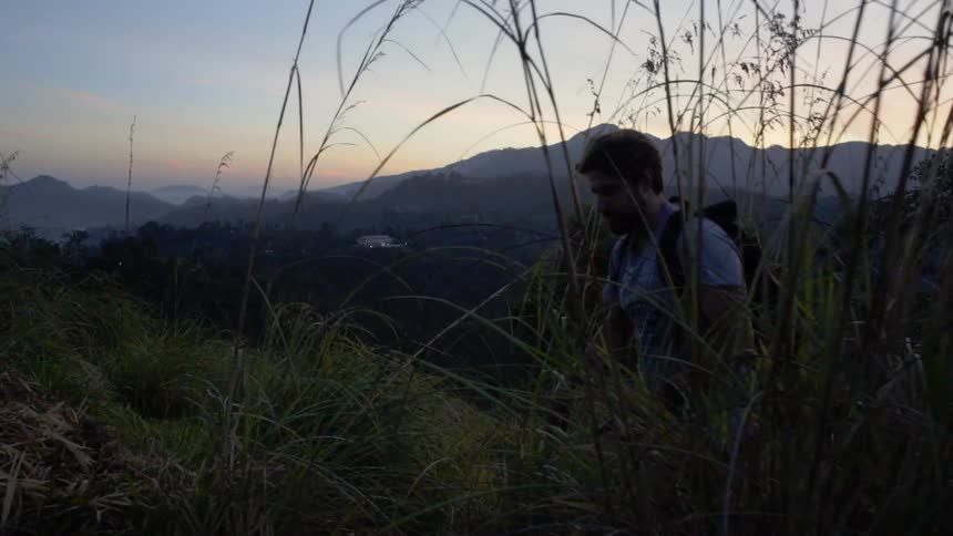 Bearded man with backpack hiking through mountains at sunset