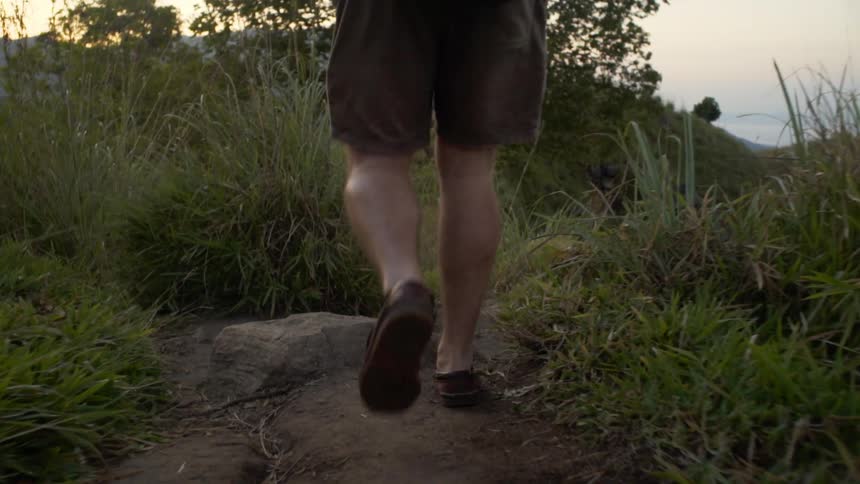 A man with shorts and a backpack hiking on a dirt path