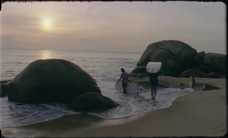 Two people with surfboards on beach at sunset
