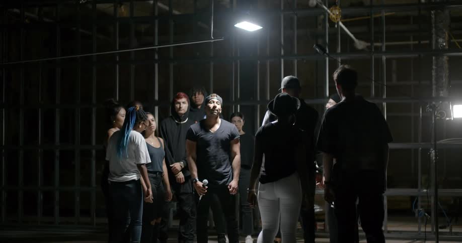 A man with a mic standing under a light surrounded by people