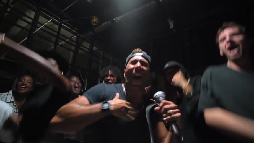 A man holding a microphone dancing while singing into the mic while other people surround him and danced with him as well