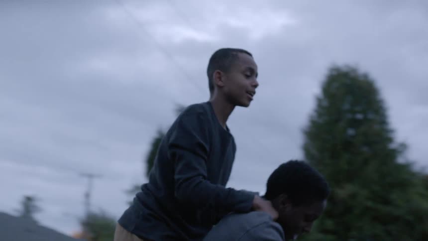Two boys ride the same bicycle in neighborhood street at sunset