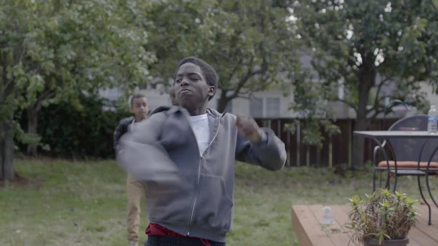 A boy walks through a yard with friends and throws a ball