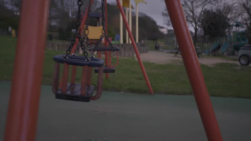 An empty playground swing moves back and forth