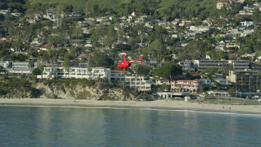 Slow motion aerial view of a red helicopter flying near the coast
