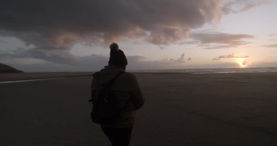A person wearing winter attire strolls across the beach to the ocean