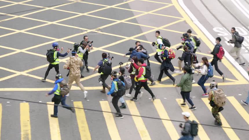 Men try to help an injured protester across the street while photographers run and surround them to get a shot