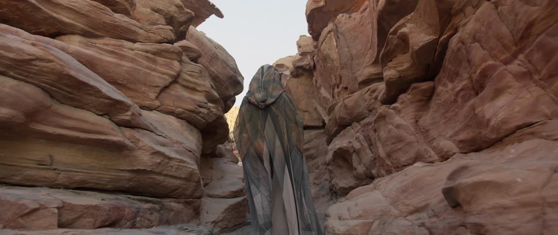 A person with a cloak walking between a canyon