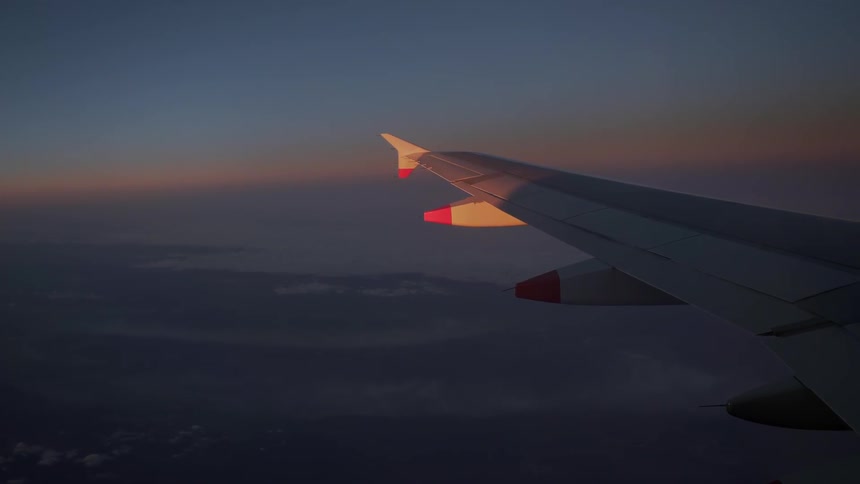 View out the window of a plane of a wing at sunset