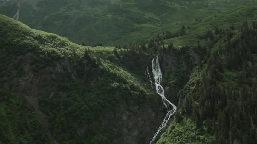 Aerial view of a waterfall streaming over grass covered mountains